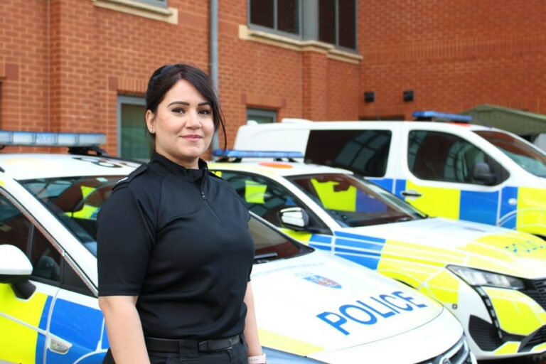 PC Manpreet Thiara is stood in front of a police car and looking into the camera. She is wearing a black polo police shirt and has her hair tied back.