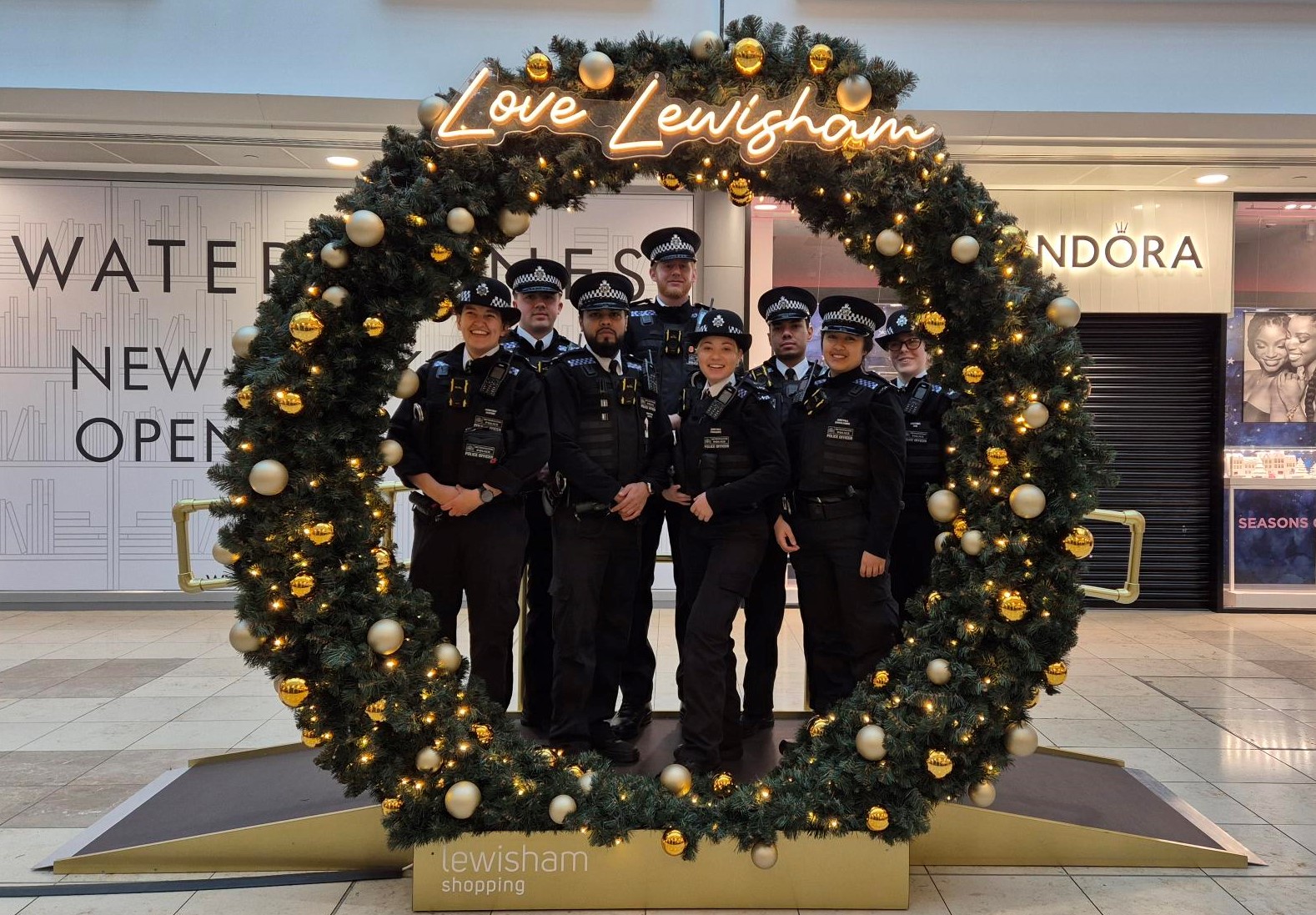 A group of officers stand under an archway designed as a festive wreath. It says 'Love Lewisham' in light-up letters at the top.