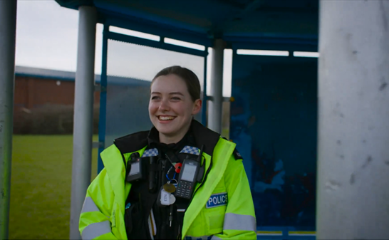 Police officer Caitlin Neal smiles at the camera, she is in a local community park and wearing a police uniform and high-vis jacket