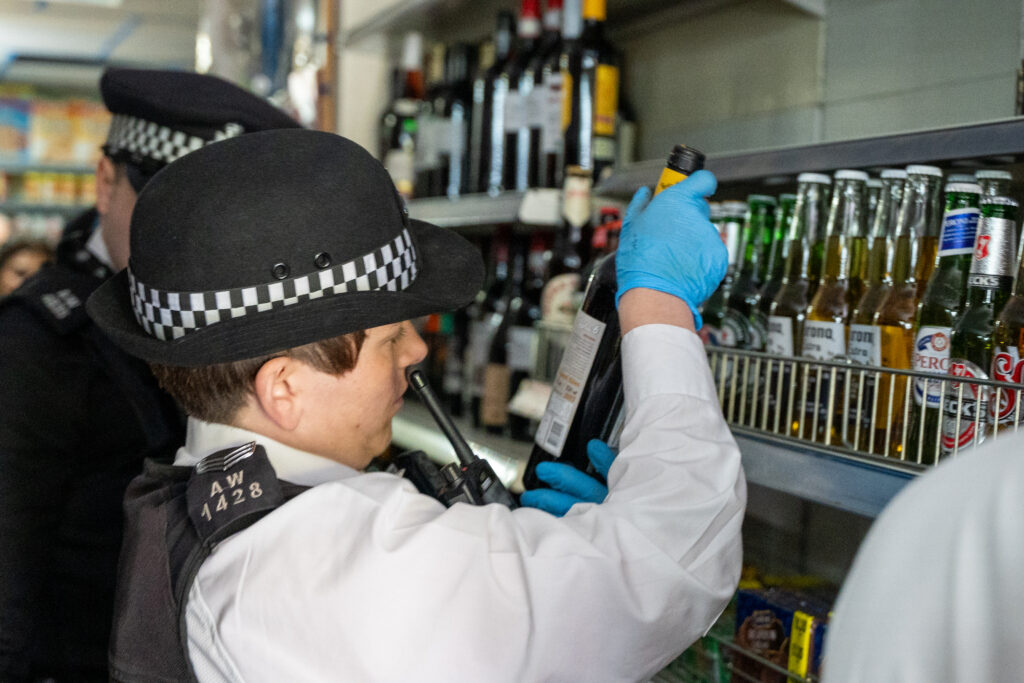 An officer wearing gloves is examining items in a corner shop