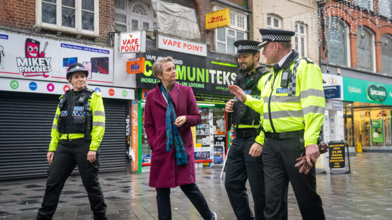 The Home Secretary Yvette Cooper walks down the street whilst talking to three uniformed police officers.