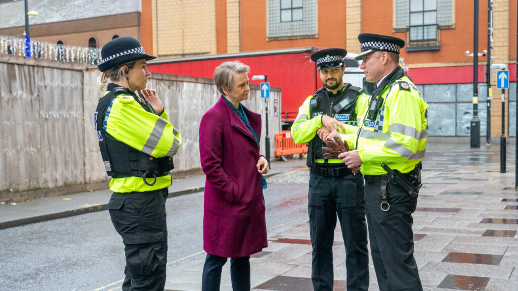 The Home Secretary Yvette Cooper stands with three uniformed police officers. They are outside and clearly chatting.