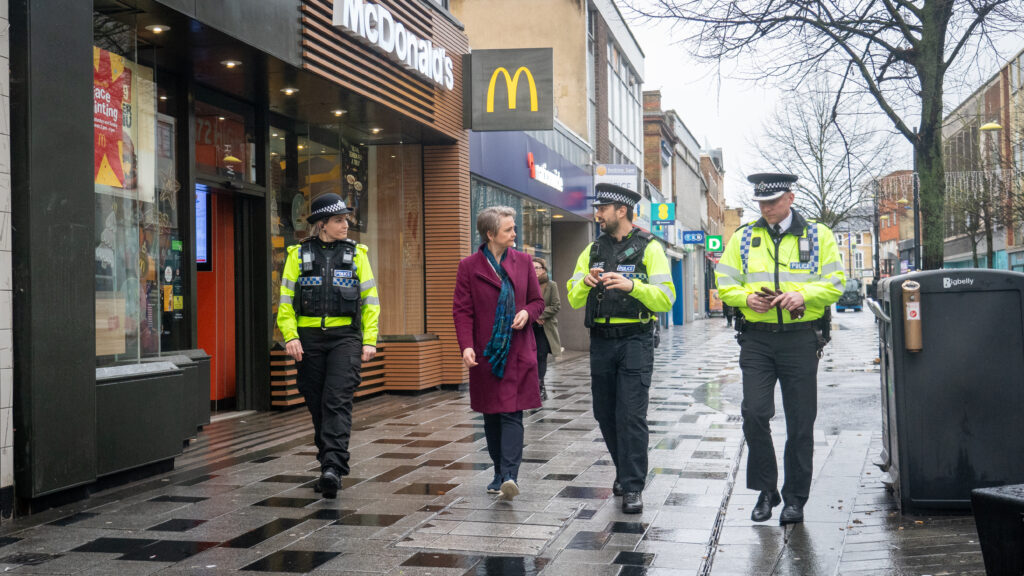 The Home Secretary Yvette Cooper walks down the street whilst talking to three uniformed police officers.