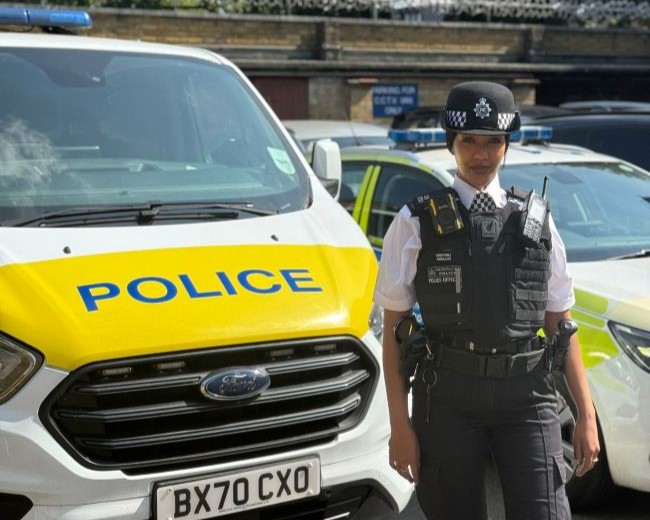 PC Farhiya Abdullahi stands in her Metropolitan Police uniform besides a police van, on a sunny day in London