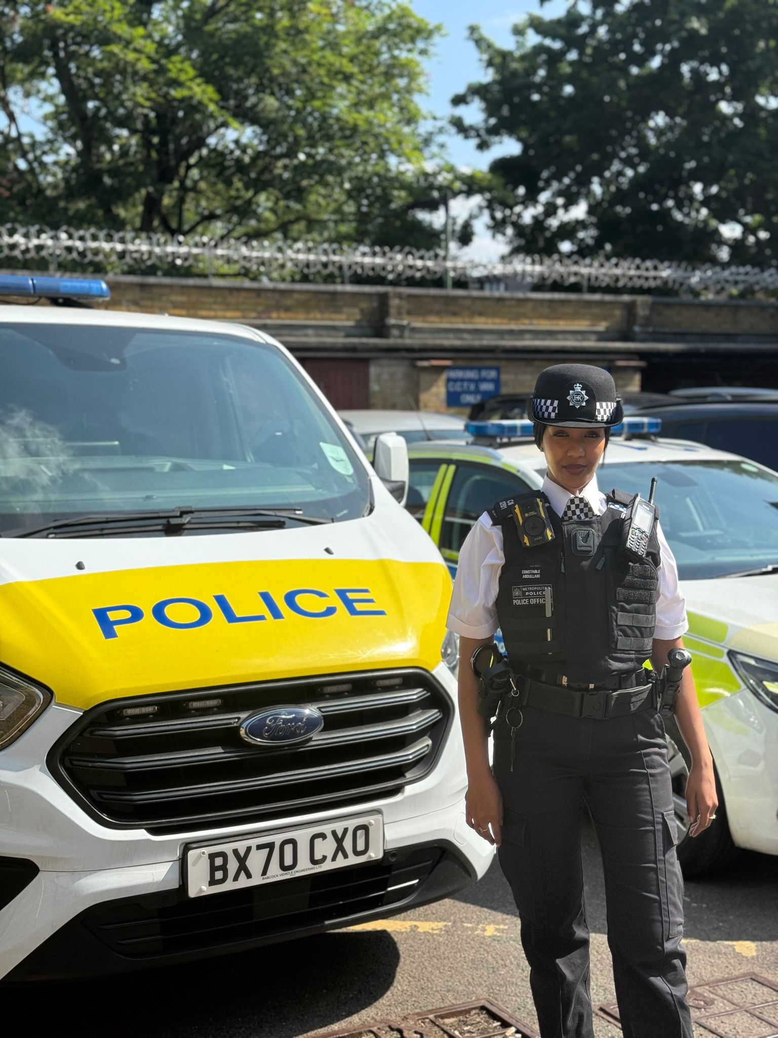 PC Farhiya Abdullahi stands in her Metropolitan Police uniform besides a police van, on a sunny day in London