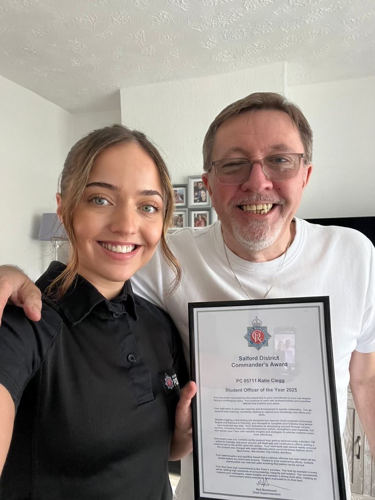 Katie stands with her Student Officer of the Year certificate. Her grandfather has an arm around her and looks proud of her achievement.